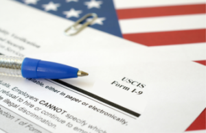 A pen on an I-9 form with an American flag in the background.