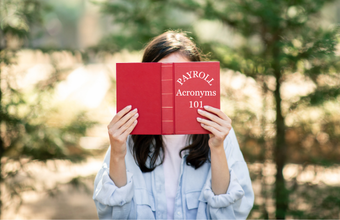 woman reading book titled Payroll Acronyms 101