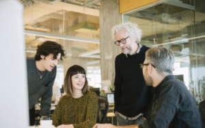 Group of 3 men and 1 woman of different generations in workplace sharing ideas.