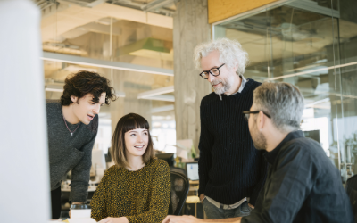 Group of 3 men and 1 woman of different generations in workplace sharing ideas.