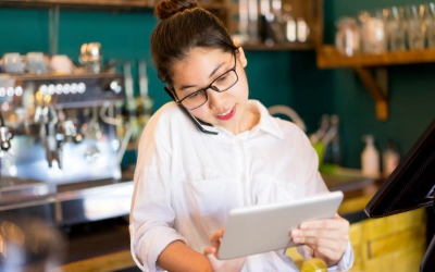 Woman as a coffeeshop worker on the phone and tablet working.