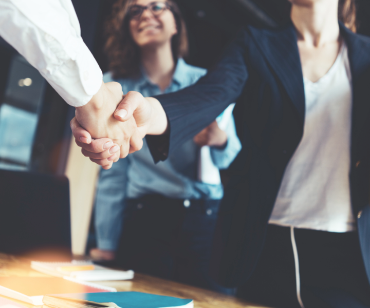 Two people shaking hands with a woman in the background