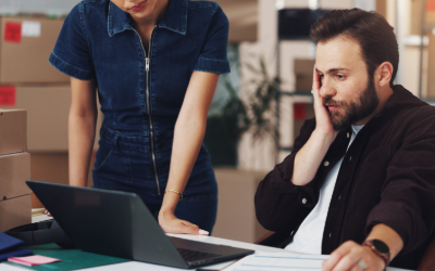 A man sitting down and next to him a woman standing looking worried at their computer