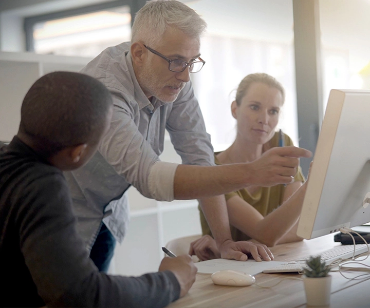 Manager teaching two new hires something on a computer