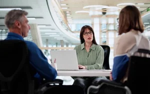 woman at laptop sitting across desk from two people